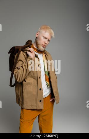 uomo albino bearded in camicia elegante giacca posa con mano in tasca e tenendo lo zaino isolato su grigio, immagine stock Foto Stock