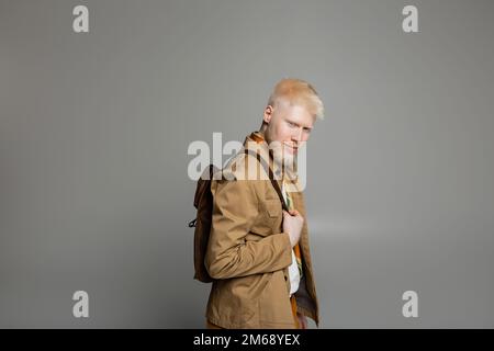 uomo albino beared in camicia elegante giacca e sciarpa di seta posa con zaino isolato su grigio, immagine stock Foto Stock