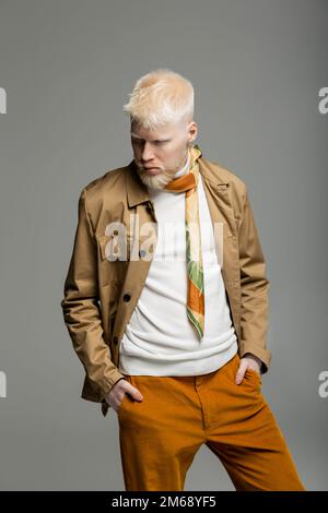 albino uomo in camicia elegante giacca e sciarpa di seta in piedi con le mani in tasche isolato su grigio, immagine stock Foto Stock