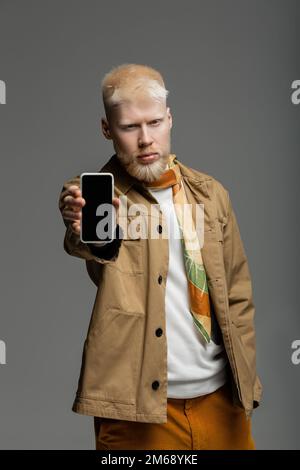 uomo albino bearded in camicia elegante giacca tenendo smartphone con schermo vuoto isolato su grigio, immagine stock Foto Stock