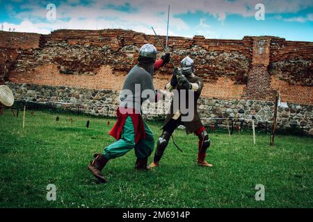Lotta di spada di due cavalieri in caschi e armatura di catena posta in scenario di castello medievale Foto Stock
