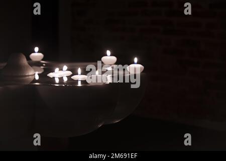 Candele galleggianti di cera che bruciano in una fontana di marmo al buio Foto Stock