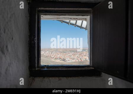 Finestra quadrata di un mulino a vento con pale e vista sulla città di Consuegra sulla rotta Don Chisciotte in Spagna Foto Stock