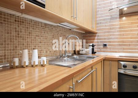 Angolo di una cucina in legno con lunghe maniglie in metallo e un muro di mattoni in argilla Foto Stock