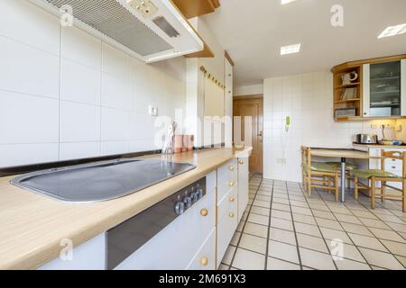 Cucina con armadietti di legno bianco con tiri di palla di legno, lungo banco in legno di faux e tavolo da pranzo con sedie di legno abbinate Foto Stock