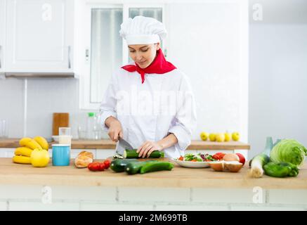 Donna proffesional cuoca in bianco uniforme tagliando verdure Foto Stock