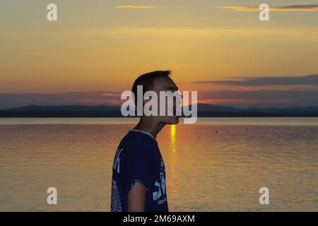 Regione di Chelyabinsk, Russia - 12 luglio 2019. Bel ragazzo sullo sfondo del tramonto sul lago. Foto Stock