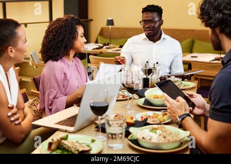 Gli uomini d'affari multirazziali stanno avendo cena di affari e discutendo il progetto in un ristorante. Foto Stock