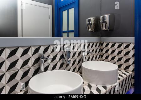 Interno del bagno con lavabo rubinetto. Bagno dal design moderno con elementi blu. Lavabo bianco e rubinetto in acciaio inox grigio lucido con Foto Stock