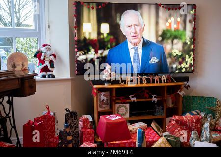 Il suo primo giorno di Natale trasmesso alla nazione dalla morte di sua madre, regina Elisabetta III in settembre, re Carlo III parla con una famiglia suburbana sulla loro TV widescreen nel loro salotto che è riempito di regali avvolti, il 25th dicembre 2022, a Nailsea, Inghilterra. Foto Stock