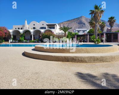 Santorini, Grecia - 26 giugno 2022: I vacanzieri sconosciuti godono squisito complesso alberghiero con piscina nel villaggio di Perissa, montagna con il monastero Profitis I. Foto Stock