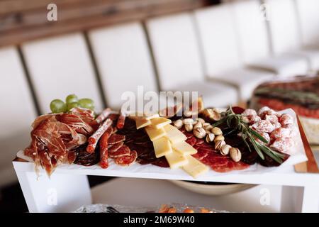 Mix di diversi spuntini e antipasti. Tapas bar. Prosciutto, salsiccia, formaggio, jamon, salame, uva, fichi e rosmarino su piatto bianco nel natale aziendale Foto Stock