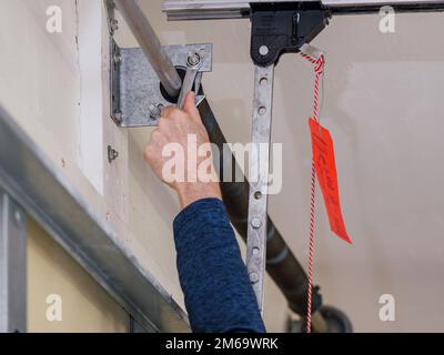 Uomo che ripara la molla a spirale della porta del garage elettrica. Installazione e regolazione del meccanismo di apertura della porta del garage a padiglione. Foto Stock