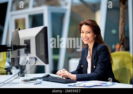 Donna d'affari di mezza età che usa il computer mentre si siede alla scrivania in ufficio. Donna professionista che lavora sul bilancio. Foto Stock