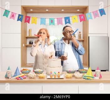 Uomo maturo e donna ad una festa di compleanno soffiando un corno dietro un bancone da cucina Foto Stock