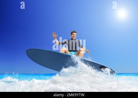 Giovane uomo in sella a una tavola da surf in mare e sorridente alla macchina fotografica Foto Stock