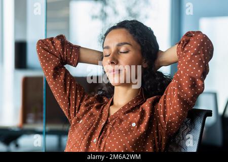 Donna ispanica business con occhi chiusi sognare sul posto di lavoro, primo piano di lavoro femminile con le mani dietro la testa pensando serio. Foto Stock