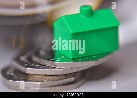 Una casa verde equilibrata su un mucchio di monete da 50 pence, mercato immobiliare, stabilità, prezzi delle case, ipoteca Foto Stock