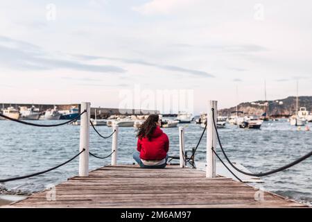 donna seduta sul molo di legno di fronte al mare Foto Stock