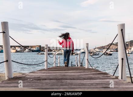 donna che cammina sul molo di legno di fronte al mare Foto Stock