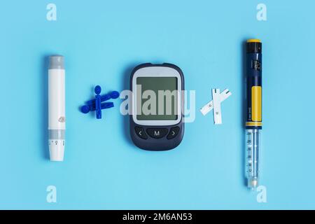 Misurazione dello zucchero nel sangue. Glucometro, penna per insulina, lancetta e striscia reattiva su sfondo blu Foto Stock