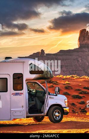 Motorhome con logo aziendale parcheggiato su strada di ghiaia di fronte alla formazione rocciosa impressionante, ago di roccia, strada panoramica nella Monument Valley, tramonto Foto Stock