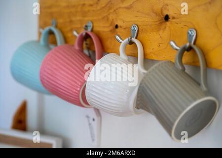 Un primo piano di tazzine colorate appese su ganci in cucina Foto Stock