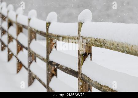 Neve che si accumula sulle rotaie e sui pali di una recinzione a tre rotaie in una scena invernale con messa a fuoco morbida Foto Stock