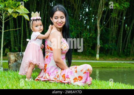 madre latina con la sua bella bruna, seduta accanto ad un lago accanto ad una gigantesca foresta di bambù, donna che guarda con orgoglio la figlia piccola. Foto Stock