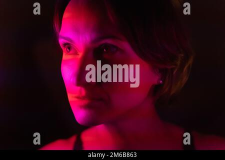 Primo piano ritratto di una giovane donna illuminato da strisce di rosa e rosso. Foto Stock
