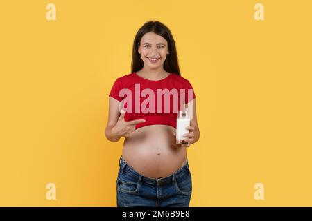 Bella giovane donna incinta che indica un bicchiere di latte in mano Foto Stock