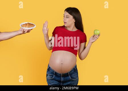 Mangiare sano durante la gravidanza. Giovane donna incinta rifiutando croissant e scegliendo Apple Foto Stock