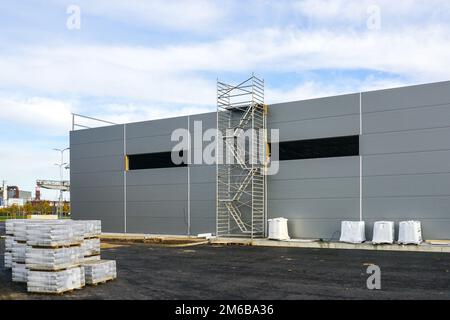 Facciata grigia a pannelli sandwich di un magazzino non finito, impalcatura tubolare multilivello, sfondo blu cielo Foto Stock
