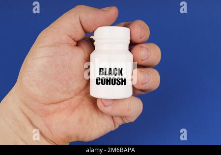 Concetto di farmacologia. Su uno sfondo blu nelle mani di un uomo è un vaso bianco con l'iscrizione - Cohosh nero Foto Stock