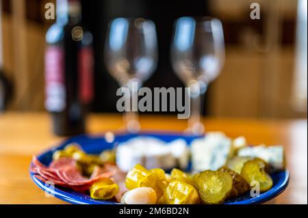 Antipasti preparati con una bottiglia di vino rosso. Un piatto ripieno di diversi tipi di formaggio, olive, peperoni, salsiccia, aglio e cetriolo e una bot Foto Stock