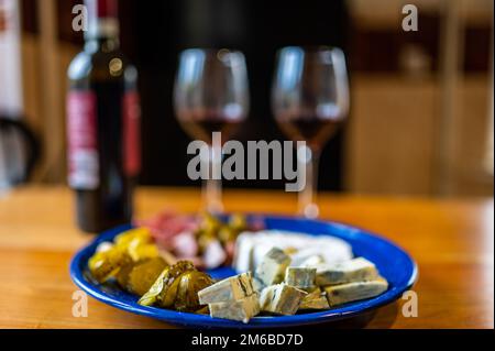 Antipasti preparati con una bottiglia di vino rosso. Un piatto ripieno di diversi tipi di formaggio, olive, peperoni, salsiccia, aglio e cetriolo e una bot Foto Stock