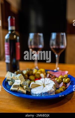 Antipasti preparati con una bottiglia di vino rosso. Un piatto ripieno di diversi tipi di formaggio, olive, peperoni, salsiccia, aglio e cetriolo e una bot Foto Stock