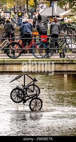 Persone che guardano le biciclette che vengono pescate fuori dal fiume ad Amsterdam Foto Stock