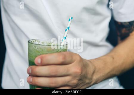 Uomo con in mano un bicchiere di frullato verde Foto Stock