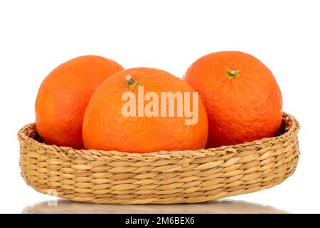 Tre tangerini organici dolci in una ciotola di paglia, macro, isolati su fondo bianco. Foto Stock