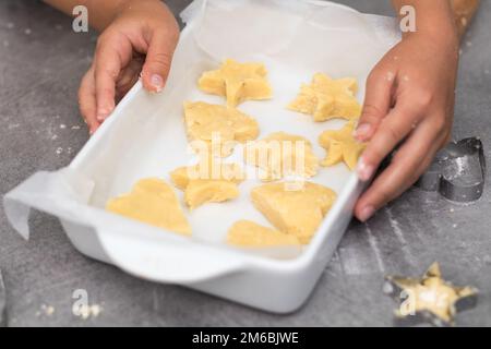 Biscotti Shortbread alla vaniglia pronti per essere cotti in vassoio, con la mano del bambino Foto Stock