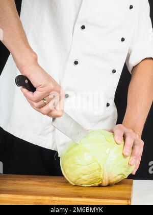 Chef professionale tenendo un affilato coltello da cucina su un cavolo cappuccio intero Foto Stock