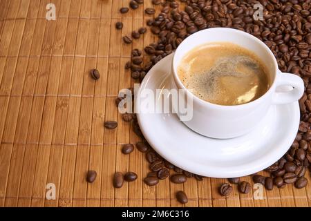 Una tazza di caffè nero sul bambù circondato da chicchi di caffè con copyspace Foto Stock