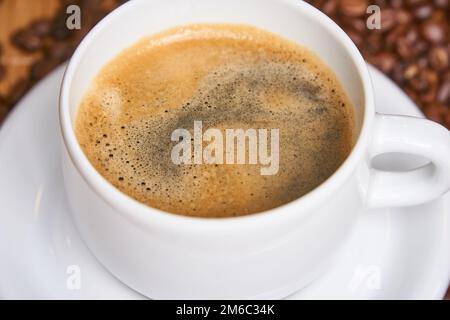 Bella tazzina di caffè circondato da chicchi di caffè su un sfondo di legno Foto Stock