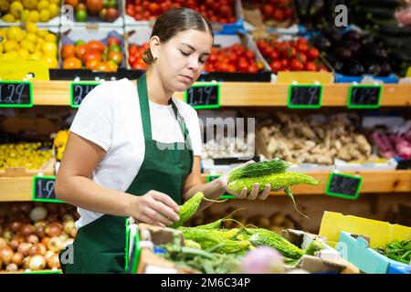 Donna sorridente dipendente del negozio di alimenti agricoli con verdure, cetriolo indiano momordica Foto Stock