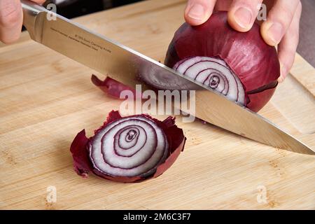 Vista sulle mani di un uomo fresco tritare la cipolla rossa per pranzo un bambù tagliere. Foto Stock