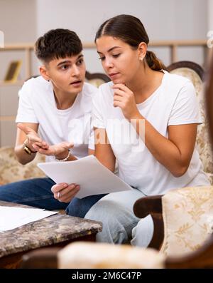 La famiglia giovane che ordina verso l'esterno le fatture di utilità insieme mentre si siede sul divano Foto Stock