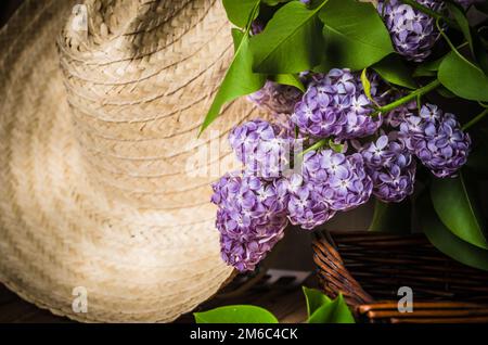 Still-life con un mazzo di lillà e un cappello di paglia, close-up Foto Stock