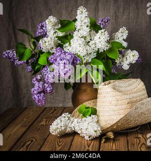 Still-life con un mazzo di lillà e un cappello di paglia, close-up Foto Stock