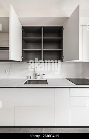 Immagine frontale di una cucina dal design moderno con mobili lisci e senza mani con interni grigi e ripiani in marmo Foto Stock